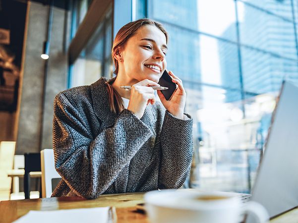 Frau telefoniert mit ihrem Handy und sitzt in einem Café.